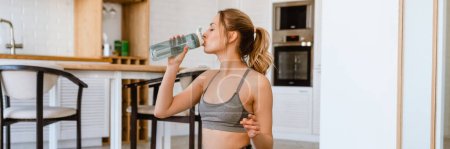 Photo for Young blonde sportswoman drinking water while training at home - Royalty Free Image