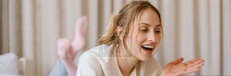 Photo for Young woman gesturing and smiling while using laptop in bedroom at home - Royalty Free Image