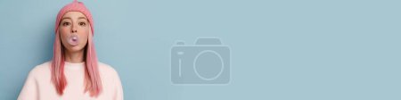 Téléchargez les photos : Jeune femme en chapeau rose soufflant chewing-gum isolé sur fond bleu - en image libre de droit