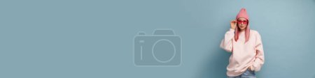 Téléchargez les photos : Jeune femme blanche aux cheveux roses portant des lunettes de soleil et regardant la caméra isolée sur un mur bleu - en image libre de droit