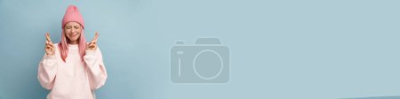 Téléchargez les photos : Jeune femme blanche aux cheveux roses fronçant les sourcils et gardant les doigts croisés isolés sur un mur bleu - en image libre de droit