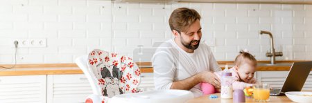 Téléchargez les photos : Père blanc souriant et jouer avec sa fille tout en utilisant un ordinateur portable à la maison - en image libre de droit