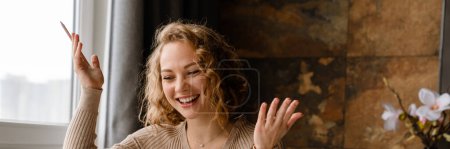Téléchargez les photos : Jeune femme blanche gestuelle et en utilisant un ordinateur portable tout en travaillant à la table à la maison - en image libre de droit