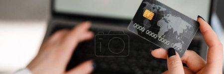 Téléchargez les photos : Gros plan d'une femme blanche magasinant en ligne via un ordinateur portable à écran vierge, tenant la carte de crédit, vue du dessus - en image libre de droit