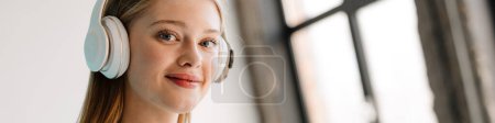 Foto de Mujer rubia joven escuchando música con auriculares y teléfono celular en el interior - Imagen libre de derechos