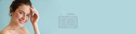 Téléchargez les photos : Femme brune à moitié nue souriante et regardant la caméra isolée sur fond bleu - en image libre de droit