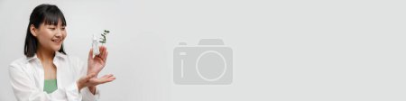 Téléchargez les photos : Jeune femme asiatique montrant sérum facial et tenant copyspace isolé sur fond blanc - en image libre de droit