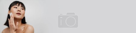 Téléchargez les photos : Jeune asiatique torse nu femme nettoyage son visage avec coton pad isolé sur fond blanc - en image libre de droit