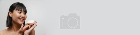Téléchargez les photos : Jeune asiatique torse nu femme souriant tout en posant avec morceau de savon isolé sur fond blanc - en image libre de droit