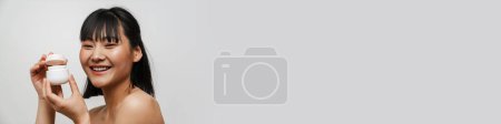 Téléchargez les photos : Jeune asiatique torse nu femme riant tout en posant avec visage crème isolé sur fond blanc - en image libre de droit