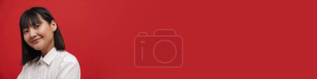 Téléchargez les photos : Jeune femme brune asiatique souriant et regardant la caméra isolée sur fond rouge - en image libre de droit