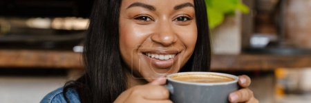 Téléchargez les photos : Femme souriante noire buvant du café alors qu'elle était assise au café - en image libre de droit