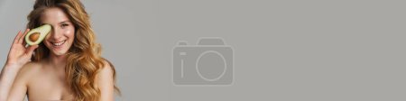 Téléchargez les photos : Femme roux blanc à moitié nue souriant tout en posant avec avocat isolé sur fond gris - en image libre de droit