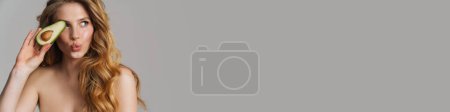 Téléchargez les photos : Femme roux à moitié nue faisant lèvre baiser tout en posant avec avocat isolé sur fond gris - en image libre de droit