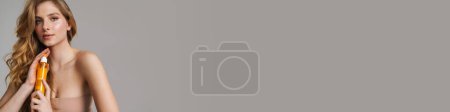 Téléchargez les photos : Femme gingembre blanc à moitié nue posant avec un produit de beauté isolé sur fond gris - en image libre de droit