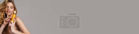 Téléchargez les photos : Femme à moitié nue montrant un geste de silence tout en montrant un produit de beauté isolé sur fond gris - en image libre de droit
