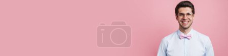 Téléchargez les photos : Jeune homme blanc portant noeud papillon souriant et regardant la caméra isolée sur fond rose - en image libre de droit