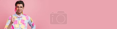 Téléchargez les photos : Jeune homme blanc avec des autocollants souriant et montrant pouce vers le haut isolé sur fond rose - en image libre de droit