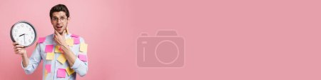 Téléchargez les photos : Excité homme brunette d'âge moyen en chemise debout recouvert de post-it autocollants sur fond mural rose montrant horloge murale - en image libre de droit