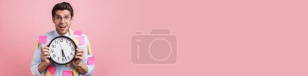Photo for Young white man with stickers exclaiming while showing clock isolated over pink background - Royalty Free Image
