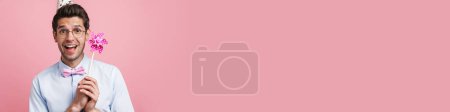 Téléchargez les photos : Jeune homme blanc portant cône de fête posant avec spinner vent fleur isolé sur fond rose - en image libre de droit