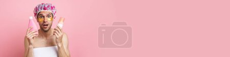 Téléchargez les photos : Jeune homme blanc portant un bonnet de douche posant avec des produits de beauté isolés sur fond rose - en image libre de droit