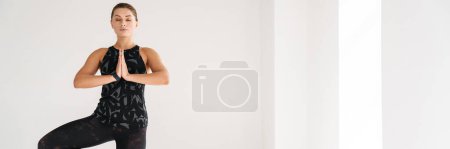 Photo for Calm young brunette woman in sportswear balancing on one foot on a fitness mat in the studio - Royalty Free Image
