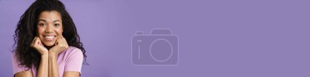 Téléchargez les photos : Gros plan d'une jeune africaine heureuse en vêtements décontractés debout sur fond violet, regardant la caméra, souriant - en image libre de droit