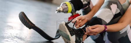 Foto de Joven deportista con prótesis atándose los cordones mientras hace ejercicio en interiores - Imagen libre de derechos
