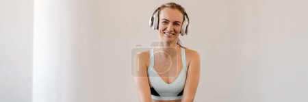Photo for Disabled happy young white sportswoman in headphones with prosthetic leg sitting on a floor in room - Royalty Free Image