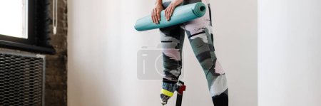 Téléchargez les photos : Jeune sportive avec prothèse posant avec tapis de fitness à l'intérieur - en image libre de droit