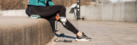 Téléchargez les photos : Jeune sportive en bonne santé avec la jambe prothétique reposant assis à l'extérieur buvant de l'eau d'une bouteille - en image libre de droit