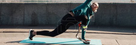 Photo for Young healthy sportswoman with prosthetic leg exercising on a fitness mat outdoors wearing headphone - Royalty Free Image
