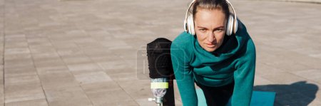 Téléchargez les photos : Jeune sportive en bonne santé avec une jambe prothétique faisant de l'exercice sur un tapis de fitness à l'extérieur portant un casque - en image libre de droit