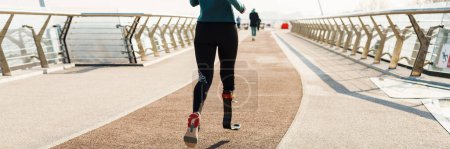 Téléchargez les photos : Jeune sportive avec prothèse en cours d'exécution tout en travaillant sur le pont de la ville - en image libre de droit