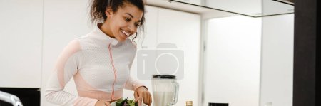 Photo for Black woman laughing and using laptop while cooking at home - Royalty Free Image