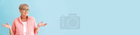 Téléchargez les photos : Européenne mature femme tenant copyspace et souriant à la caméra isolé sur fond bleu - en image libre de droit