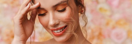 Téléchargez les photos : Jeune femme souriante avec de longs cheveux bouclés bruns nus posant sur un fond mural floral - en image libre de droit
