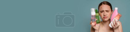 Téléchargez les photos : Femme torse nu au gingembre avec boutons fronçant les sourcils tout en montrant des cosmétiques isolés sur fond bleu - en image libre de droit