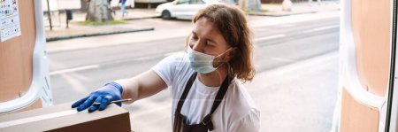 Photo for Young white cafe worker in face mask taking delivery outdoors - Royalty Free Image