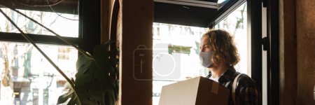 Photo for Young white cafe worker in face mask taking delivery indoors - Royalty Free Image