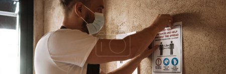 Photo for Young white cafe employee in face mask affixing placard while working indoors - Royalty Free Image