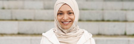 Téléchargez les photos : Moyen-Orient femme en hijab en utilisant un téléphone mobile tout en travaillant à l'extérieur - en image libre de droit