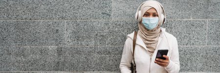Foto de Mujer de Oriente Medio en mascarilla usando teléfono móvil mientras está al aire libre - Imagen libre de derechos