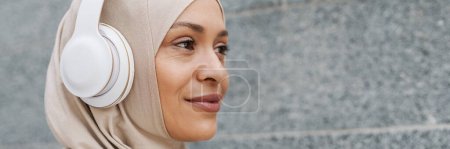Photo for Middle eastern woman in hijab listening music with wireless headphones outdoors - Royalty Free Image