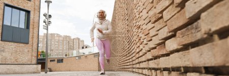 Foto de Mujer de Oriente Medio en hijab escuchando música con auriculares y corriendo al aire libre - Imagen libre de derechos