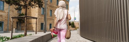 Foto de Vista trasera de una mujer musulmana de mediana edad en ropa deportiva y hijab caminando por una calle - Imagen libre de derechos