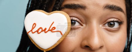 Photo for Young black woman exclaiming while posing with heart cookie isolated over blue background - Royalty Free Image