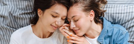 Foto de Un retrato de la feliz pareja de chicas lesbianas cogidas de la mano en la cama en la sala de luz - Imagen libre de derechos