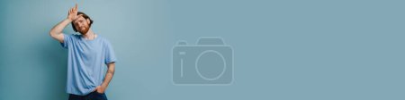 Téléchargez les photos : Jeune homme roux avec barbe pointant doigt vers le haut isolé sur fond bleu - en image libre de droit